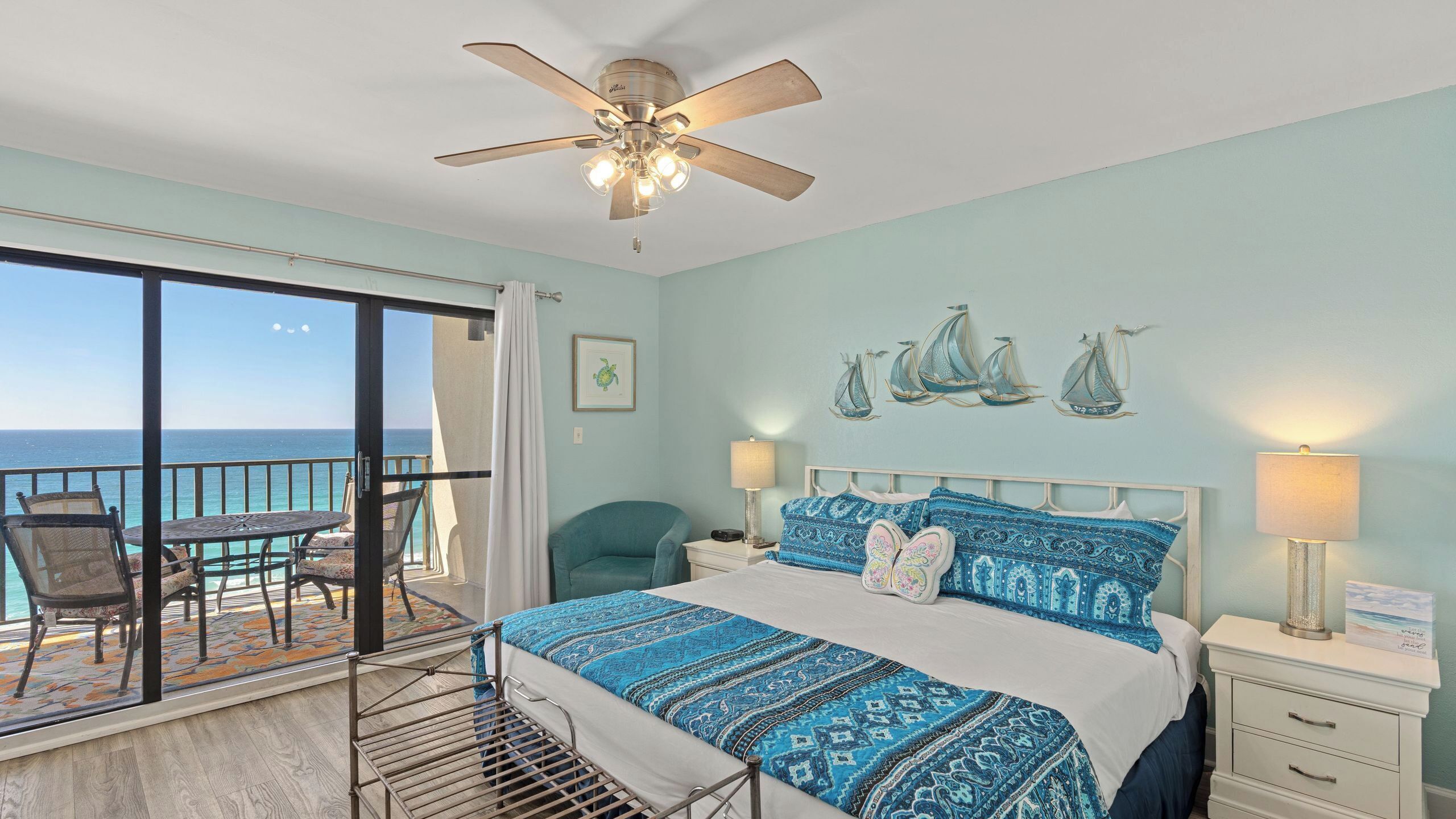 A bedroom with a bed, nightstands, a ceiling fan, and a view of the ocean.