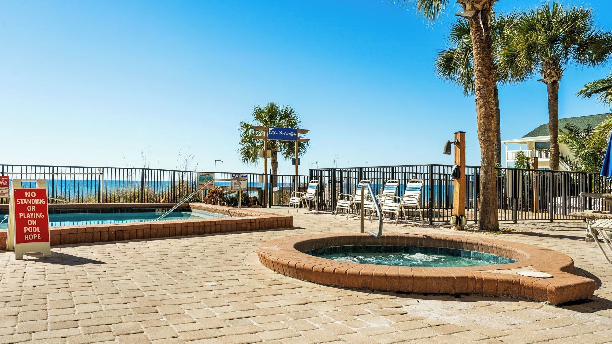 A pool area with a no standing or playing on pool rope sign, lounge chairs, and a hot tub.