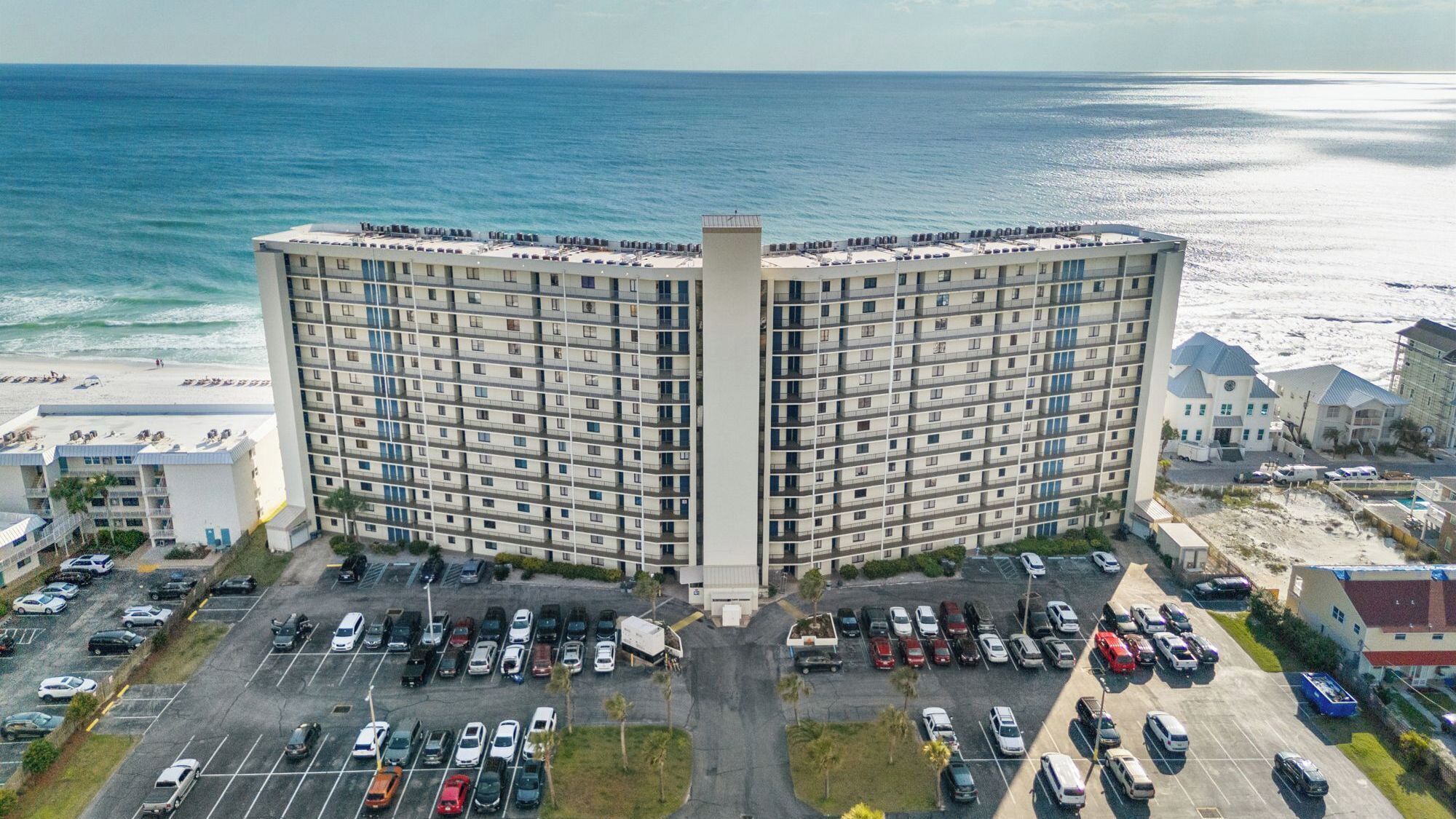 A high-rise hotel with a central courtyard, parking lot, and beachfront view.