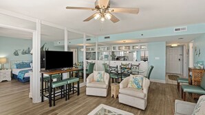 A spacious living area with a television, dining table, chairs, and a ceiling fan. - Gull Watch by Avantstay Beachfront Condo (Panama City Beach)
