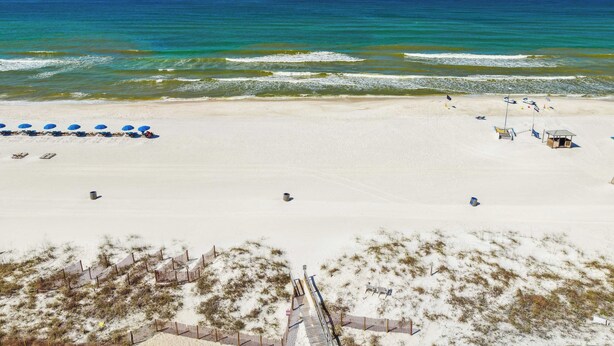 A beach with a sandy shore, a few umbrellas, and a small structure. - Aqua Horizon by Avantstay Pool, Near the Beach (Panama City Beach)