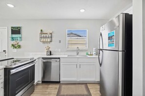 A modern kitchen with white cabinets, stainless steel appliances, a built-in oven, and a refrigerator. - Aqua Horizon by Avantstay Pool, Near the Beach (Panama City Beach)