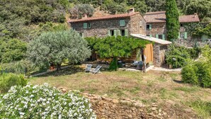 Una casa de piedra con un patio, rodeada de vegetación y una colina.