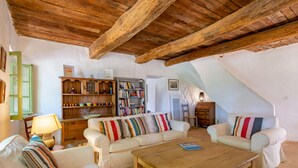 Una sala de estar acogedora con techo de madera, sofás blancos, una mesita de centro y una estantería llena de libros y adornos.