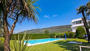 Une piscine entourée d’une pelouse bien entretenue, un ciel bleu azur et un paysage vallonné en arrière-plan.