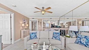 Un salon avec un canapé beige, une table basse agrémentée d’objets décoratifs et un ventilateur de plafond.