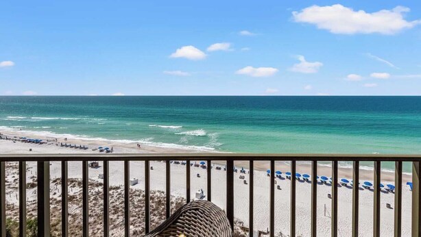 Une vue sur la plage depuis un balcon doté d’une balustrade, avec des parasols de plage et un ciel dégagé.