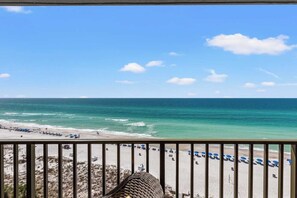 A beach view from a balcony with a railing, beach umbrellas, and a clear sky. - Beachfront Breeze by Avantstay Beachfront Condo (Panama City Beach)