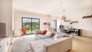 Un salon moderne comprenant un canapé, un téléviseur, un coin repas et un balcon offrant une vue sur la verdure.