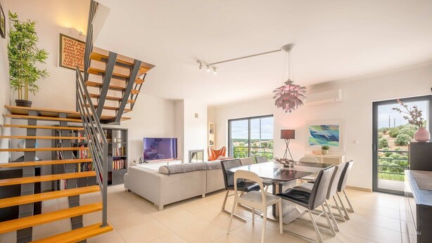 Un salon moderne doté d’un escalier, d’un coin repas et d’une grande fenêtre donnant sur l’extérieur.