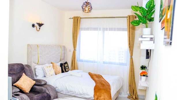 A hotel room with a bed, a sofa, a small round table, and a potted plant. - Studio Sleeps 2 with 24hr Check-in (Nairobi)