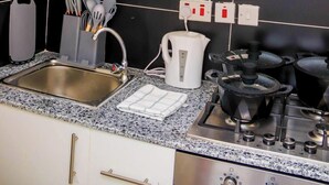 A kitchen with a granite countertop, stainless steel sink, and a gas stove. There are cabinets above the counter and a coffee machine on the wall. - Studio Sleeps 2 with 24hr Check-in (Nairobi)