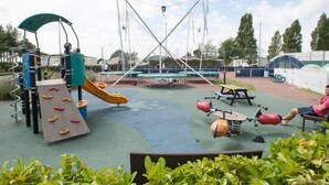 Ein Spielplatz im Freien mit verschiedenen Spielgeräten, darunter eine Rutsche, eine Kletterwand und Schaukeln.