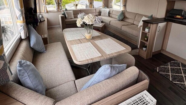Ein gemütliches Wohnmobil-Interieur mit einer Sofagarnitur, einem Esstisch mit Untersetzern und einer Küchenzeile inklusive Fernseher.
