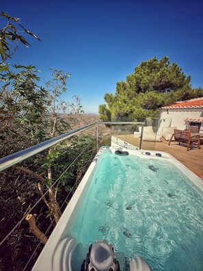 A hot tub with a clear view of the surrounding landscape, including trees and a distant view of hills.