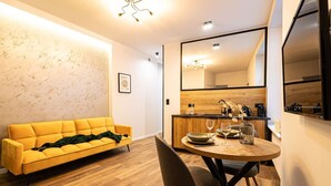 A modern living room with a yellow sofa, a dining table with chairs, a kitchen area, and a large mirror. - 2HomeRent Estrella 10 | Old Town | Spacious (Torun)
