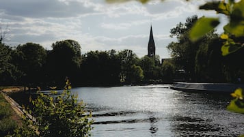 A river with a church spire in the distance, surrounded by trees and greenery.