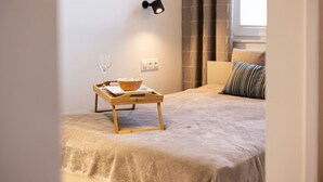 Un dormitorio con una cama, una mesita de noche con un tazón de cereal y un vaso, una lámpara de pared y una ventana con cortinas.
