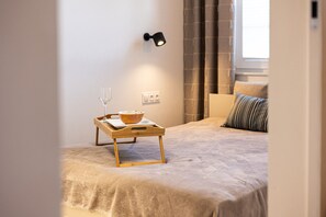 Une chambre à coucher avec un lit, une table de chevet sur laquelle se trouvent un bol de céréales et un verre, une lampe fixée au mur et une fenêtre avec des rideaux.