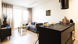 Una sala moderna con un sofá, una mesa de centro, un comedor con una pequeña isla y una cocina con isla negra y luces colgantes.