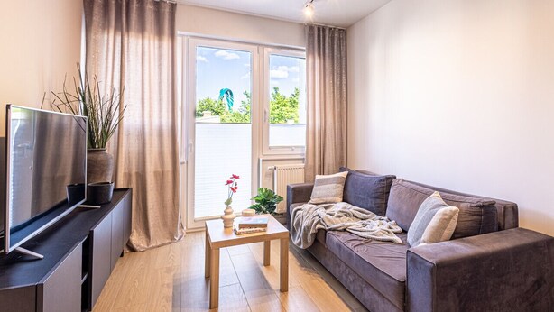 Una sala de estar moderna con un sofá, una mesa de centro, un televisor y una ventana con cortinas.