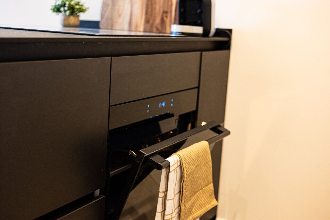A black kitchen with a built-in oven and a towel hanging on a rack.