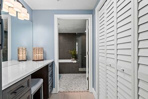 A modern bathroom with a white vanity, a glass shower enclosure, and a walk-in closet with white sliding doors. - Shoreline Serenity by Avantstay Beachfront + Views! (Panama City Beach)