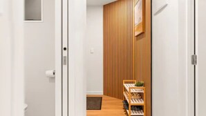 A hallway with a wooden slat wall, a small seating area with a chair and a plant, and a shoe rack.