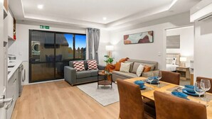 A modern hotel room with a sofa, dining table, and a view through a glass door.
