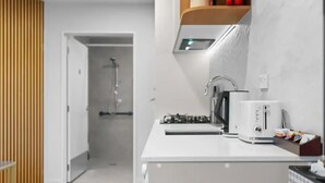 A modern kitchen with a white countertop, a kettle, a toaster, and a shelf with a plant and a red item.