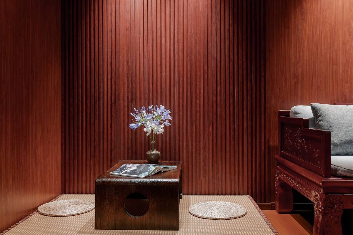 A wooden room with a small table, a vase with flowers, and a bed with pillows.