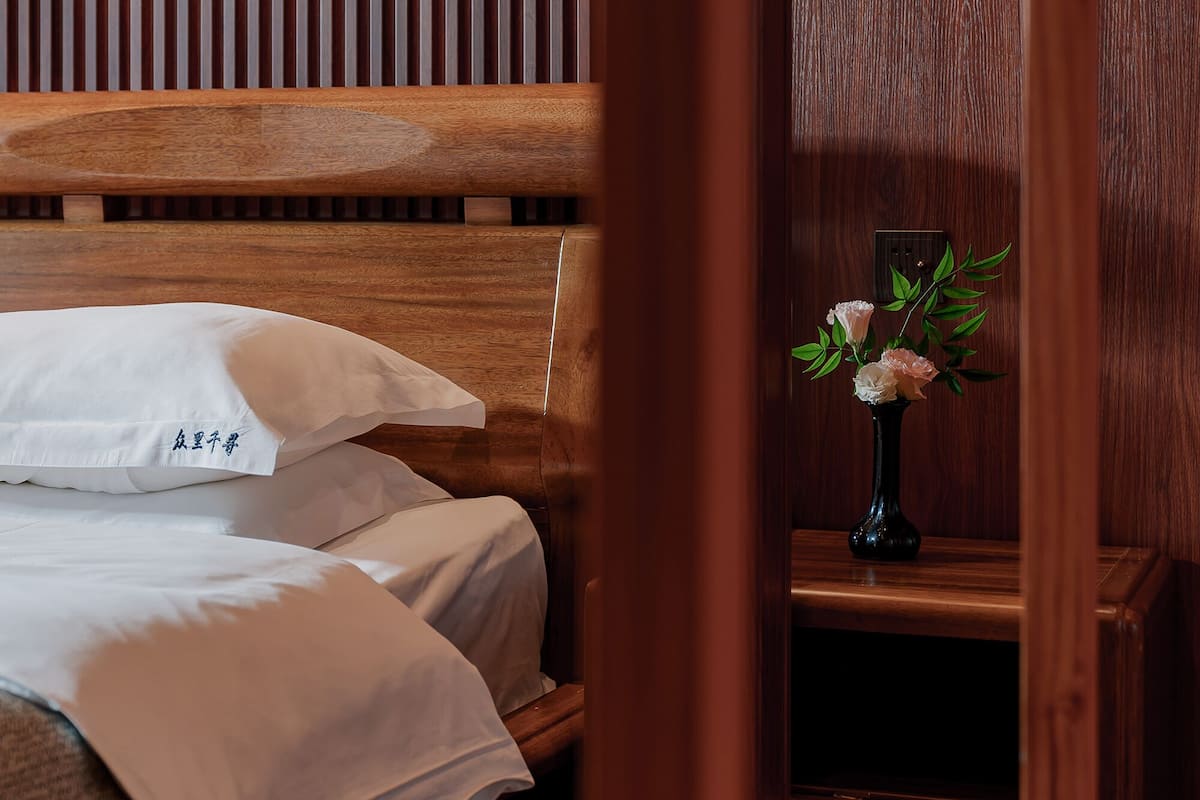 A wooden bed with white bedding, a small vase with flowers, and a wooden panel wall.