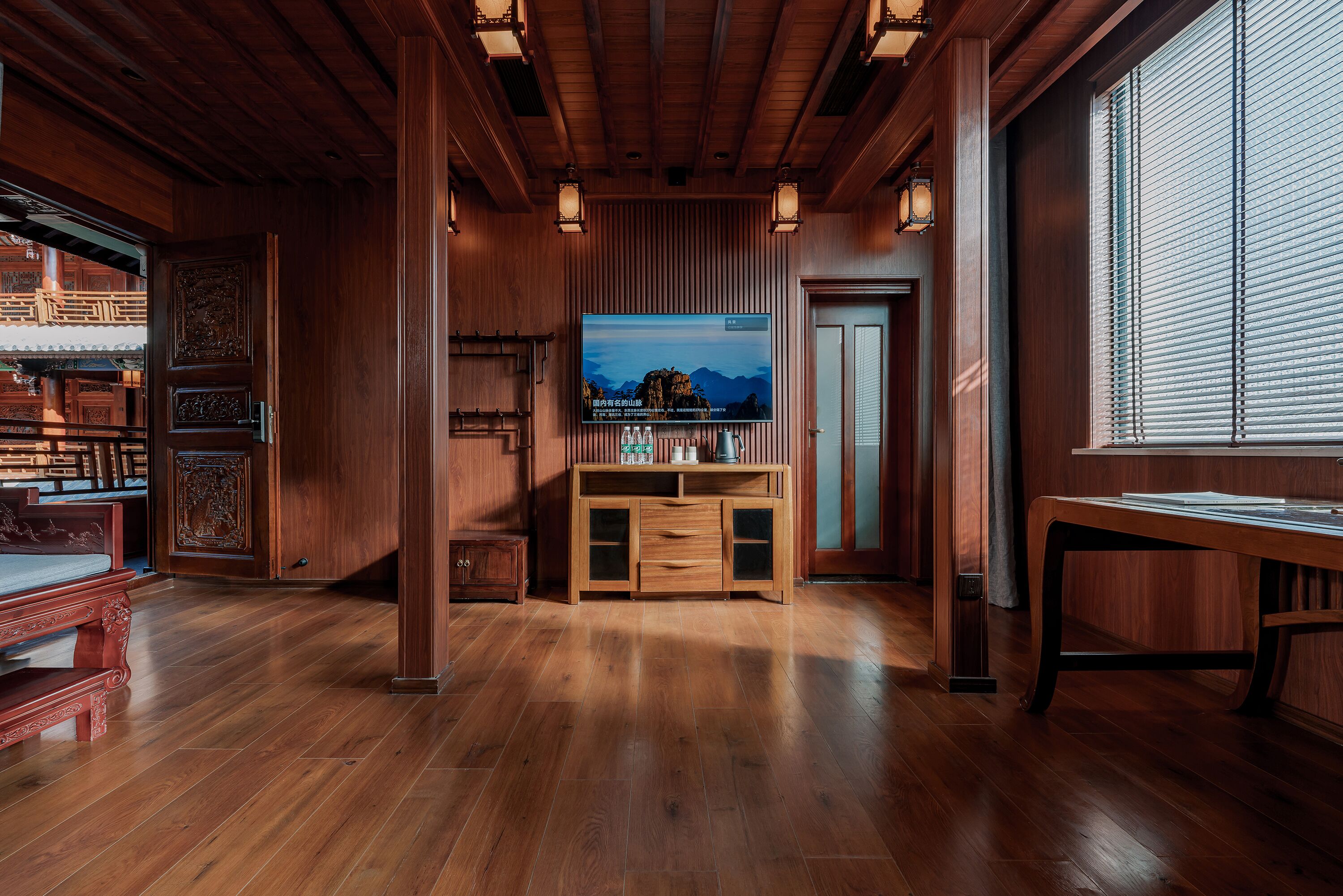 A wooden-paneled room with a large flat-screen TV, wooden furniture, and a window with blinds.