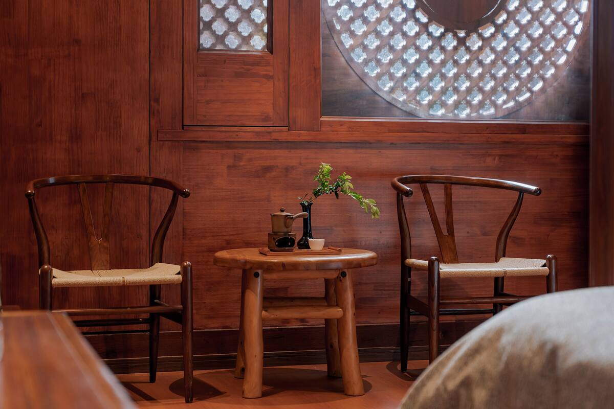 A wooden room with two chairs and a small table, a window with a lattice design, and a plant on the table.