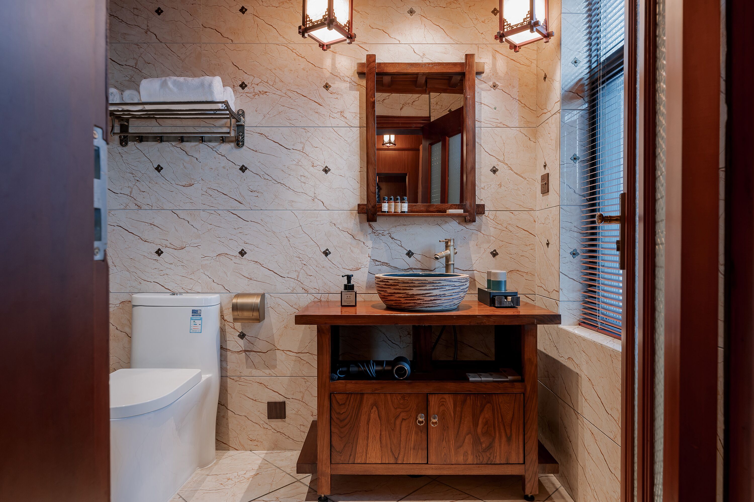 A bathroom with a marble wall, a wooden vanity, a sink with a bowl, a toilet, and a towel rack.