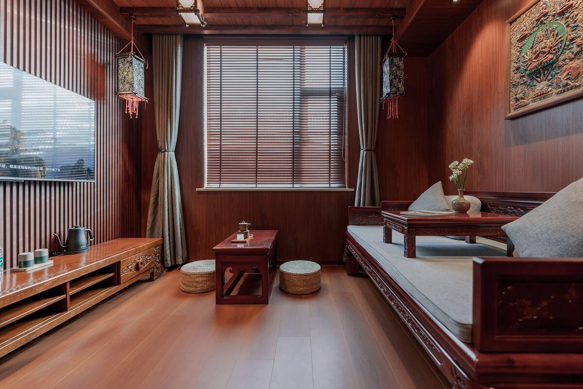 A traditional wooden room with a sofa, a small table, a window with blinds, and a decorative hanging lantern.