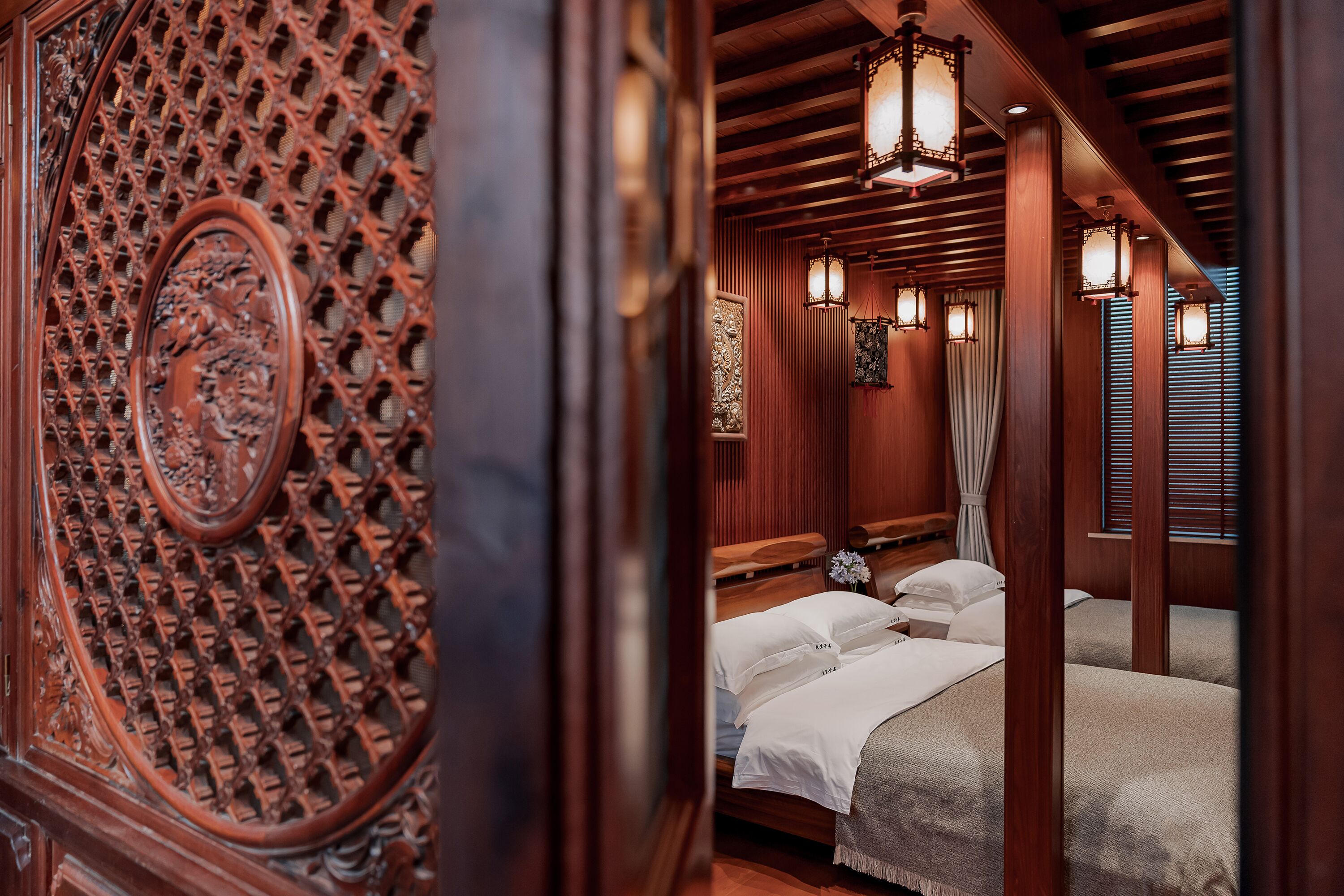 A traditional wooden room with a lattice partition, two beds with white linens, and hanging lantern-style lights.
