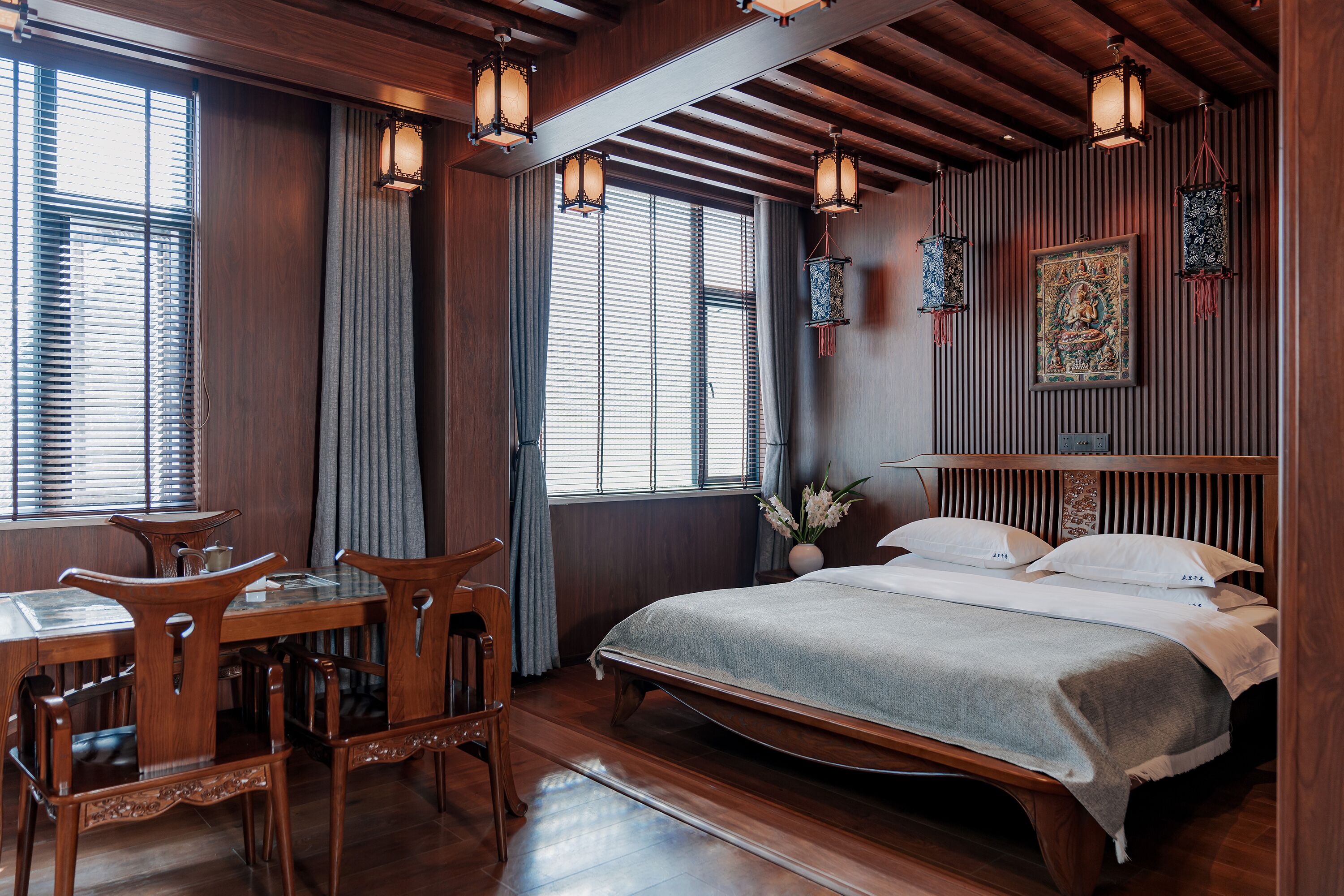 A traditional room with a wooden bed, a dining table with chairs, and a large window with curtains.