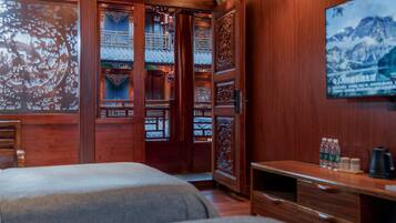 A traditional wooden room with a bed, a desk, and a TV on the wall.