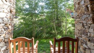 Two wooden chairs facing a stone wall with a view of a forested area.