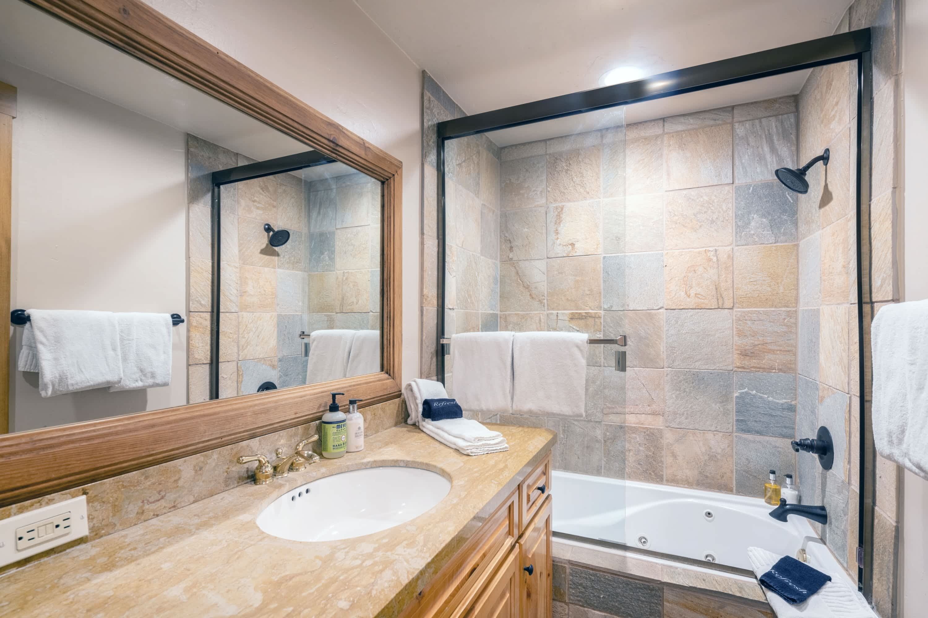 A bathroom with a large mirror, a sink, a bathtub, and a shower area.