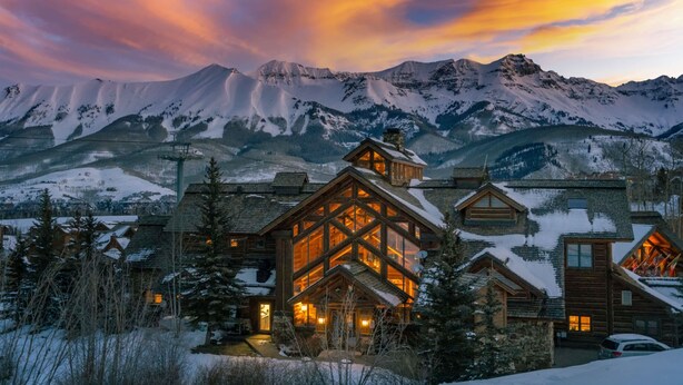 A log cabin hotel with a large central room and multiple smaller rooms, surrounded by snow-covered mountains and a sunset sky. - 2BR Ski-In, Ski-Out Telluride Condo (Telluride)