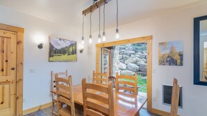 A dining area with a wooden table and chairs, a stone wall, and two paintings on the walls. - 2BR Ski-In, Ski-Out Telluride Condo (Telluride)