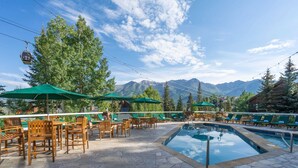 Un espace piscine agrémenté de chaises longues et de parasols, entouré d’un sol en pierre, avec des montagnes en toile de fond.