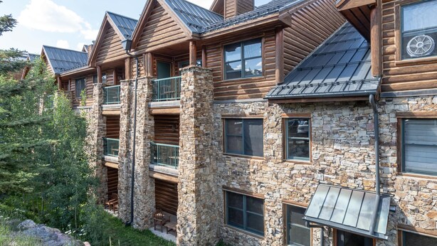 Une cabane en rondins à plusieurs étages, agrémentée de pierres apparentes, de balcons et d’un auvent en métal.
