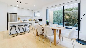 Una cucina moderna con mobili bianchi, un frigorifero in acciaio inossidabile e una zona pranzo con tavolo rotondo e sgabelli da bar.