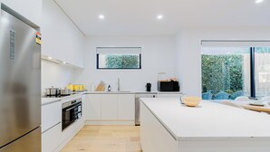 Una cucina moderna con mobili bianchi, un frigorifero in acciaio inossidabile, un forno integrato e una grande isola con una ciotola.
