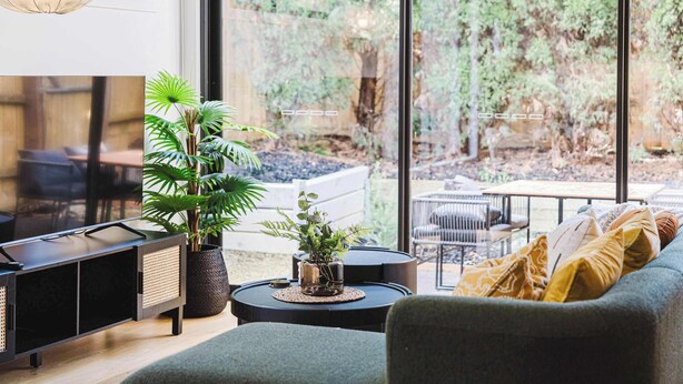 Un soggiorno moderno con divano, tavolino e mobile TV. Grande finestra con vista su un giardino.