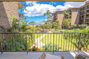 A balcony with a view of a well-maintained lawn, palm trees, and a building with multiple balconies.