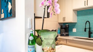 A kitchen counter with a bottle of Pellegrino water, a bag of Honolulu Cookie Company mini bites, a thank you card, and a potted orchid. - Hip Hawaiian Oceanfront Vistas (Kihei)